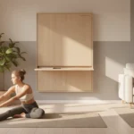 Woman stretches on a yoga mat in a small apartment living room, where a closed fold-down desk blends into the wall.